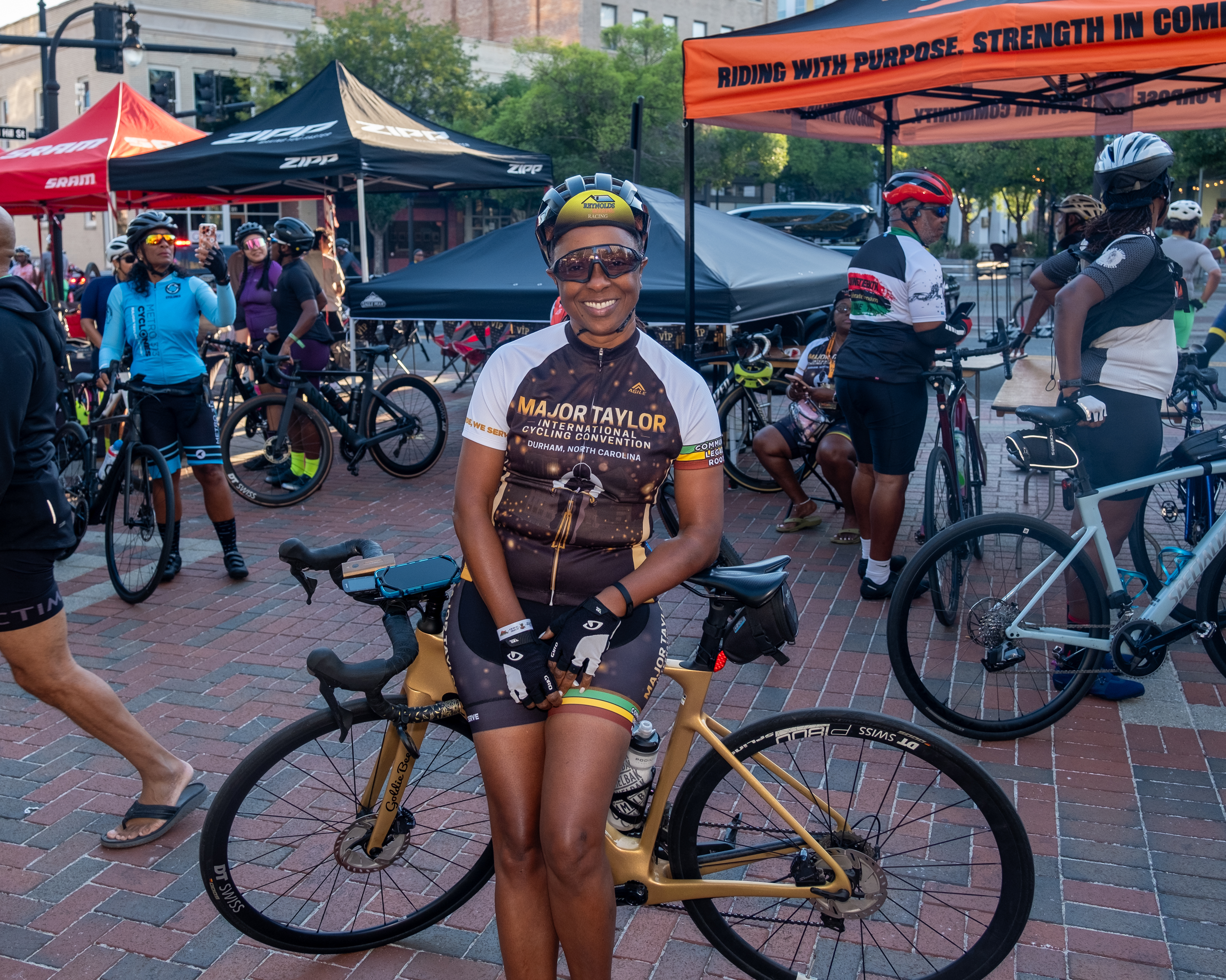 Cyclist wearing the 2026 MTICA Major Taylor International Cycling Convention official jersey standing with a gold road bike at CCB Plaza in Durham NC